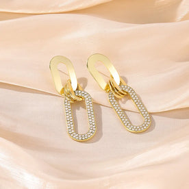 Gold earrings with diamond accents on a soft pink fabric background