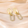Gold earrings with diamond accents on a soft pink fabric background
