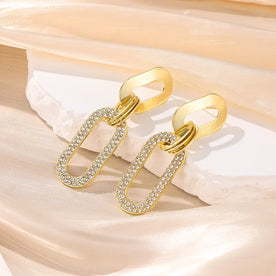 Gold chain earrings with clear stones on a beige fabric background