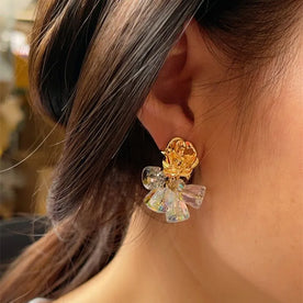 Close-up of a person wearing a decorative earring with a gold flower and clear bow design.