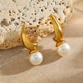 Gold earrings with pearl drops on a textured beige surface