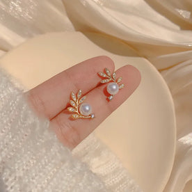 Gold earrings with pearls on a hand against a soft beige background